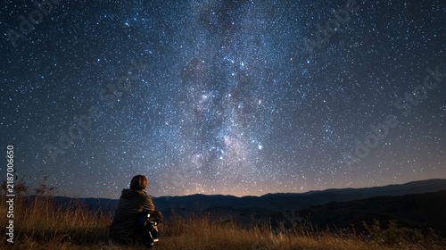 A serene stargazer contemplatively seated on a hillside at night, observing a magnificent star-filled sky, surrounded by the tranquil beauty of nature and distant mountain silhouettes, evoking a sense