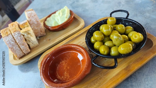 Traditional green olives served with rustic bread and a creamy dip on wooden boards, authentic Mediterranean appetizer and tapas scene.