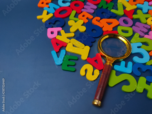 Gold brass magnifying glass placed over scattered colorful wooden letters and numbers against a dark blue background