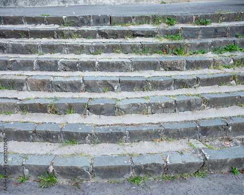 Obraz na płótnie Old weathered stone steps with weeds growing through joints, showing worn urban infrastructure, neglected maintenance, pedestrian access, masonry and aging public space