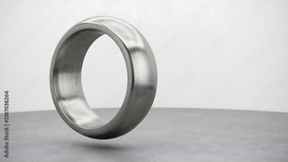 Obraz premium A single metallic ring with a smooth, polished surface floating above a grey surface against a plain, light-colored studio background