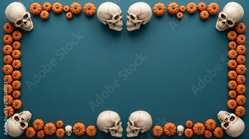 Halloween mini pumpkins and skulls border flat lay on deep teal background, spooky banner design with copy space