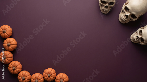Halloween pumpkins and skulls asymmetric layout flat lay on dark purple background, spooky banner design with copy space