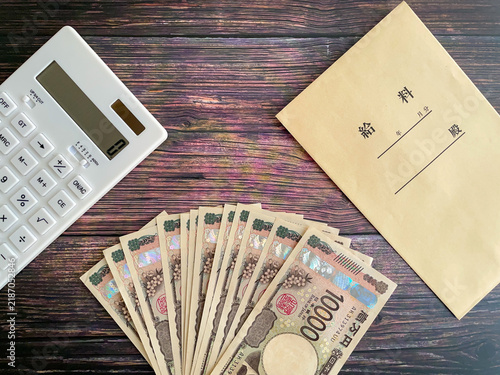 Fototapeta 木製テーブルの上に置いた紙幣と給料袋と白い電卓
