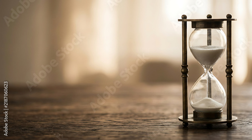 Vintage hourglass on a rustic wooden table with white sand flowing, representing time passing and management concept