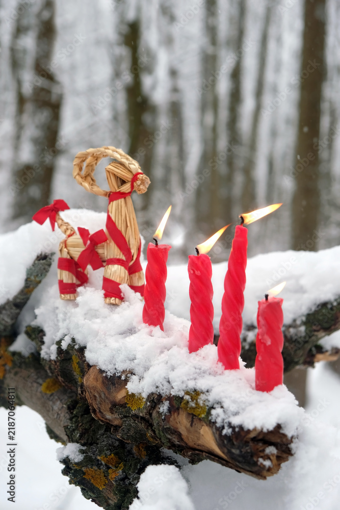 Obraz premium straw Yule Goat and burn red candles on snowy tree in winter forest. festive decor, traditional symbol of Scandinavian, Northern European Yule, Christmas holiday. witchcraft, magic ritual for Yuletide