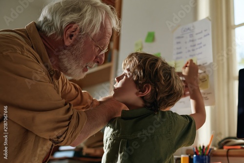 Grandfather helping young boy write goals on paper at home desk