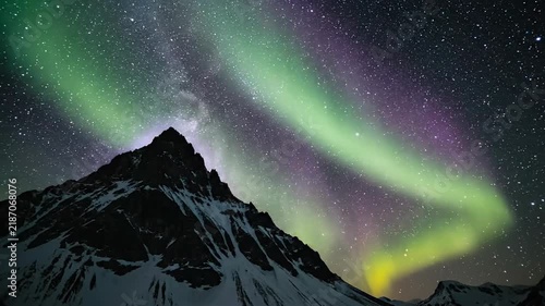 Static low angle wide shot of emerald green and violet aurora over snowy mountain peak