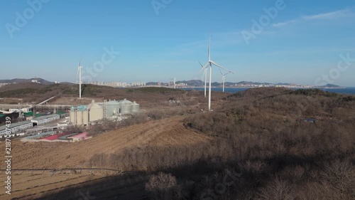 Aerial view of wind turbines and industrial factory in a winter landscape with leafless vegetation and clear sky, highlighting energy production in China.