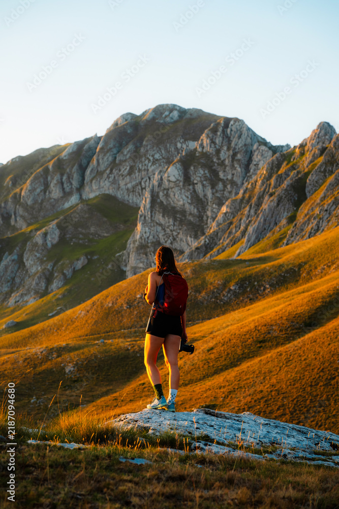 Obraz premium Young woman standing on a mountain peak at sunset, arms open or enjoying the view, embracing nature and freedom in the mountains in Durmitor National Park, Montenegro.