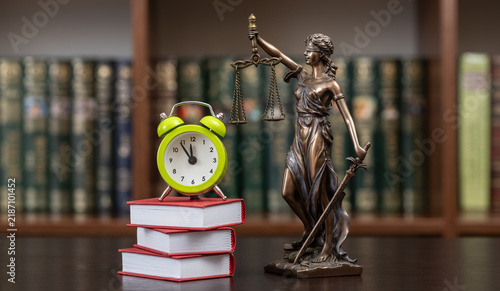фотографія A figure of Themis, books, and an alarm clock against the backdrop of a bookshelf