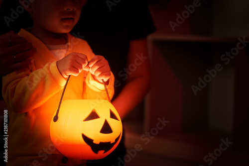 Child holding glowing Halloween pumpkin bucket lantern at home