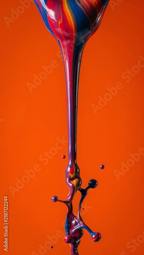 Colorful paint splashing and pouring on orange background. Vibrant blue red and yellow liquid swirls in vertical motion