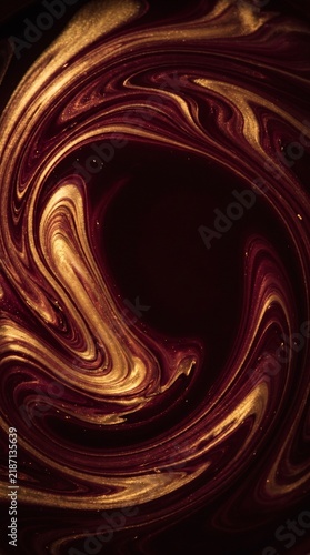 A mesmerizing abstract swirl of deep red and golden liquid creating a dynamic, organic pattern.