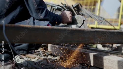 Builder with disk saw cuts hollow structural section in parts at construction site closeup. Man worker prepares metal beam details outdoors