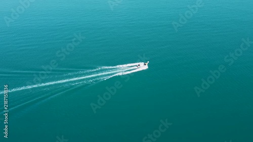 Fast fishing boat moving across the sea, aerial drone view. Speed boat sailing on the open ocean water. Drone footage of a fishing vessel leaving a wake in the sea.