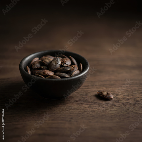 Dark Coffee Beans in Black Bowl on Wooden Surface.