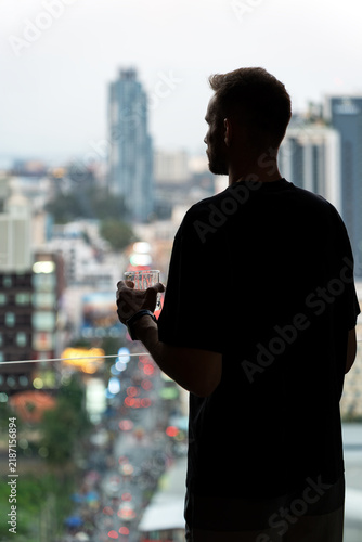 Foto Man Holding Drink And Looking Out Window At City