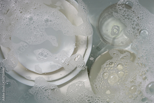 Dirty white tableware submerged in clear water for cleaning.
