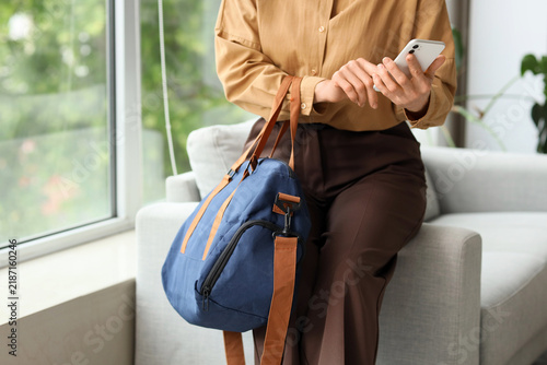 Mature businesswoman with sports bag using mobile phone in office