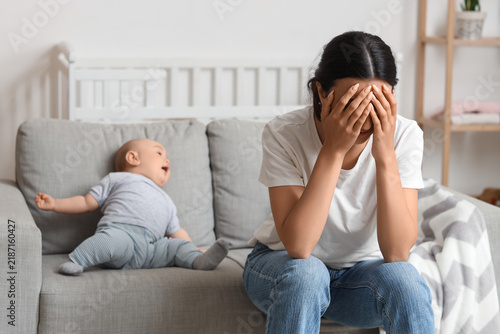Upset mother suffering from postnatal depression with her baby on sofa at home