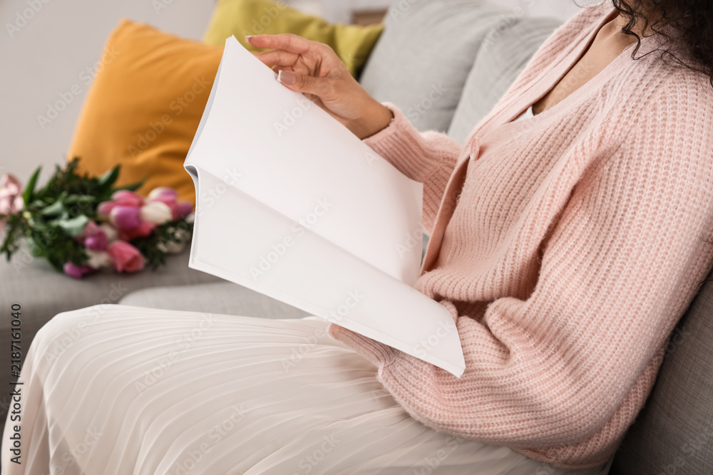 Obraz premium Young woman reading blank magazine at home on spring day, closeup