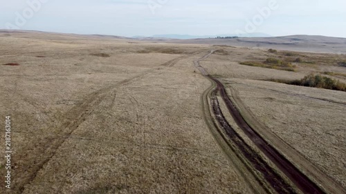 Field destroyed by vehicles with deep tire tracks. Drone shot of a ruined dry grassland landscape with wheel ruts. Worn dirt path with deep tire tracks winding through a barren field.