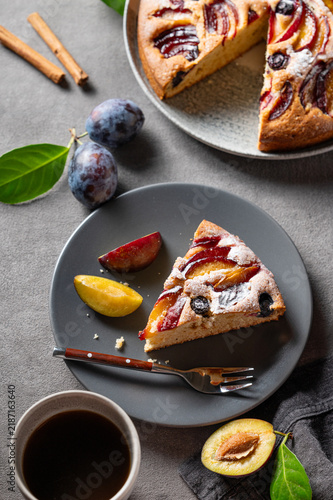 Slices of plum pie with fresh fruits and a cup of coffee on a dark table