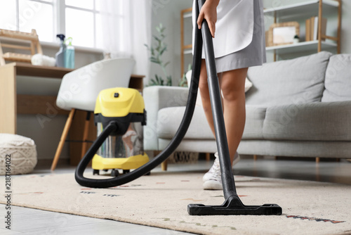 Young chambermaid vacuuming carpet in hotel room
