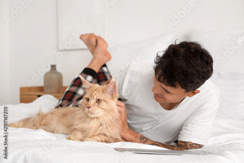 Handsome young happy man with cute Maine Coon cat lying in bedroom at home