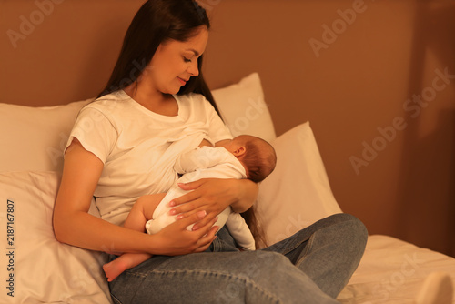 Mother breastfeeding her baby on bed at night