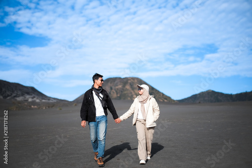 Romantic Asian couple holding hands walking on Mount Bromo's Sea of Sand during a sunny day trip in East Java, Indonesia