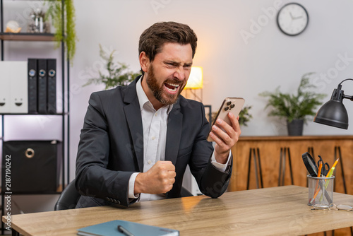Картината върху платно Middle-aged businessman at home office spends money on online lottery casino smartphone app groans as luck fails