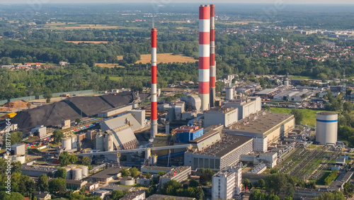 Aerial view of the coal-fired power plant with its prominent red and white striped chimneys, industrial buildings, and large coal storage piles in Warsaw, Masovian Voivodeship, Poland.