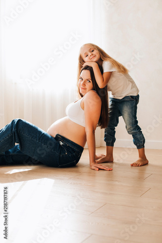 Pregnant mother sitting on the floor with her young daughter leaning affectionately on her shoulder. Tender family moment at home filled with love, connection and anticipation