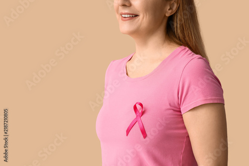 Mature woman with pink ribbon on beige background, closeup. Breast cancer awa...