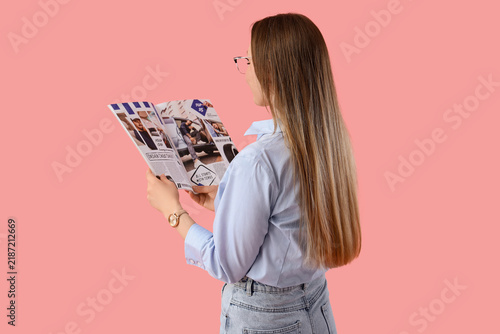 Beautiful young woman in eyeglasses reading magazine on pink background
