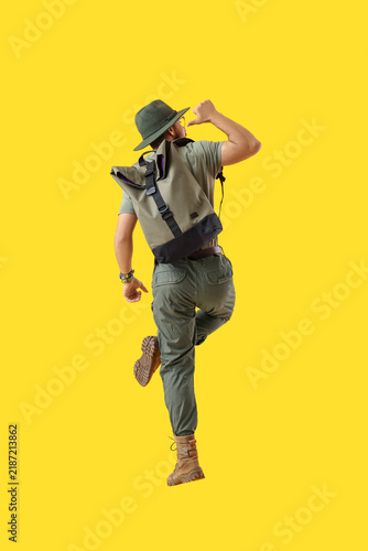 Jumping male traveler on yellow background, back view