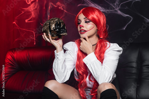 Foto Young woman shows Halloween spirit with clown makeup and red hair while holding