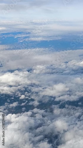Clouds and sky view from an airplane flying over a beautiful landscape during a clear day. This shows clouds and the sky as seen from an airplane during a flight over a landscape. The view is bright a