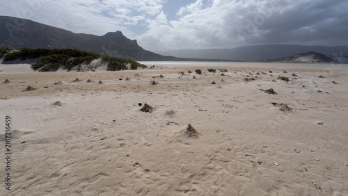 Foto Remote sandy coast beneath dramatic mountain clouds