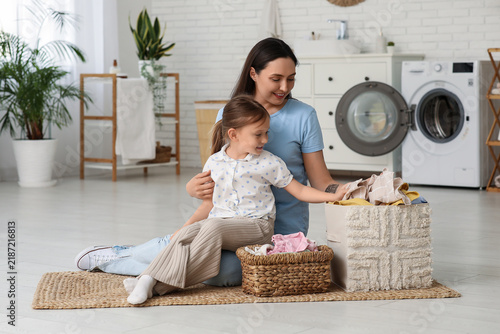 Young woman and her little daughter with two baskets full of laundry at home