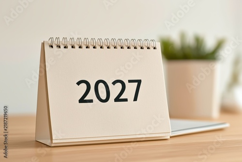 Desktop calendar displaying 2027 beside a small plant, annual planning, organized workspace, fresh start, New Year schedule.