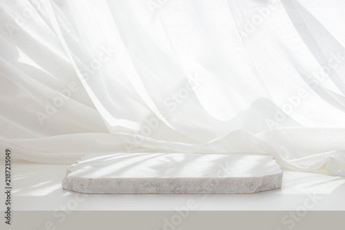 White empty marble podium in dappled sunlight on table with elegant draped curtain fabric background