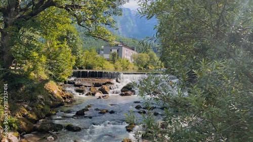 Scenic mountain river with rushing rapids and small cascades in Lofer, Austria, surrounded by lush green forest and Alpine mountains. Peaceful summer nature landscape with flowing water