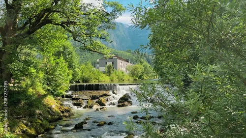 Scenic mountain river with rushing rapids and small cascades in Lofer, Austria, surrounded by lush green forest and Alpine mountains. Peaceful summer nature landscape with flowing water.