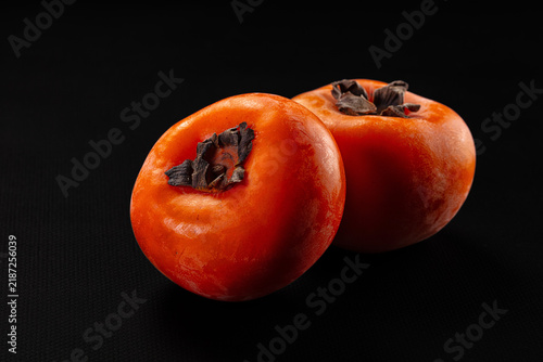 Obraz na plátne Two ripe orange persimmons with dark calyx on black background, smooth skin text