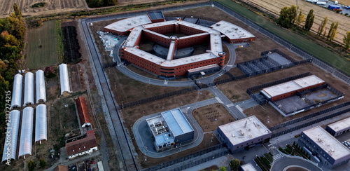 Aerial view of the prison octagon complex with surrounding security fences, agricultural greenhouses, and auxiliary buildings in Pancevo, Serbia.