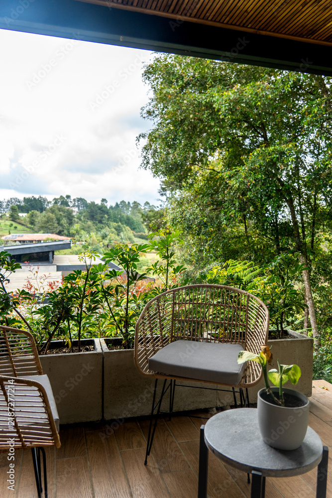 Obraz premium Balcony seating with wicker chairs and potted plants overlooking a green hillside