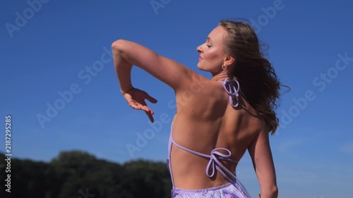 Beautiful Woman In Purple Dress Posing On A Sunny Riverside Beach. Dancing And Relaxing During Summer Vacation.